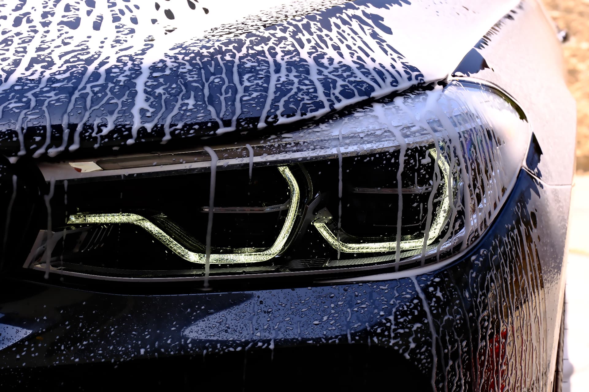 Foam covering a dark BMW headlight during a wash